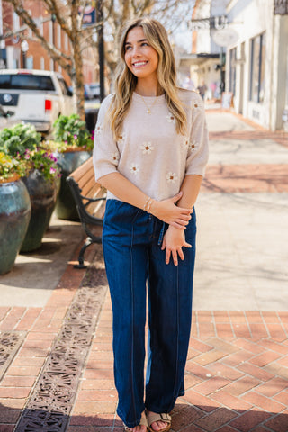 Woman in a beige sweater and dark, blue jeans 