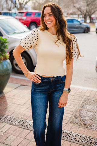 Woman wearing a beige top with polka dot sleeves and blue jeans 