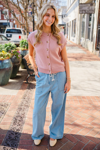 Woman wearing a mauve, pink sleeveless cardigan and blue jeans 